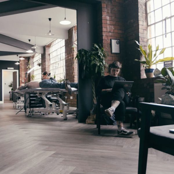 A tattoo consultant sits in the waiting area of the Birmingham tattoo studio. In the background you can see the tattoo area.
