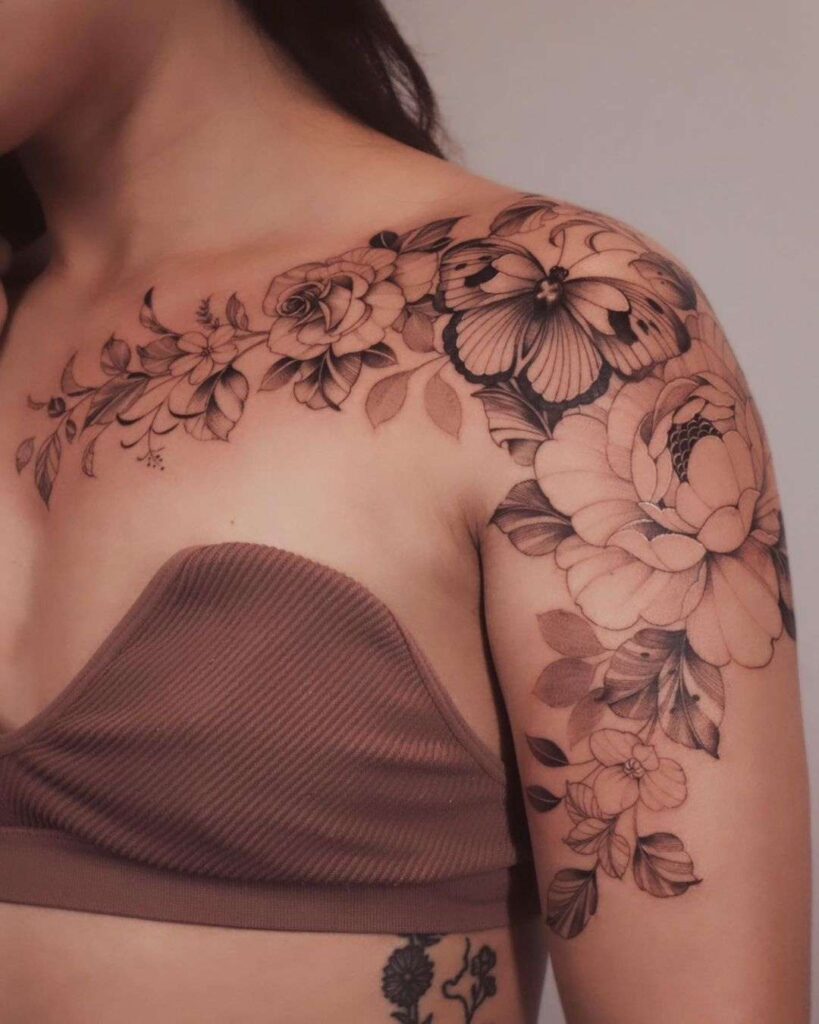 woman with a fineline floral tattoo cascading across her collar bone, going across her shoulder and down her arm. Tattoo shows peonies and a butterfly. 