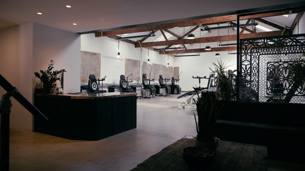 Empty wide shot of London tattoo studio. Image shows reception desk, reception area with wooden table and sofas and 5 tattoo chairs.