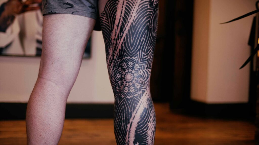 The back of Joe's impressive leg sleeve showing abstract, distressed black lines, covering the whole of his leg with a mandala in the back of his knee