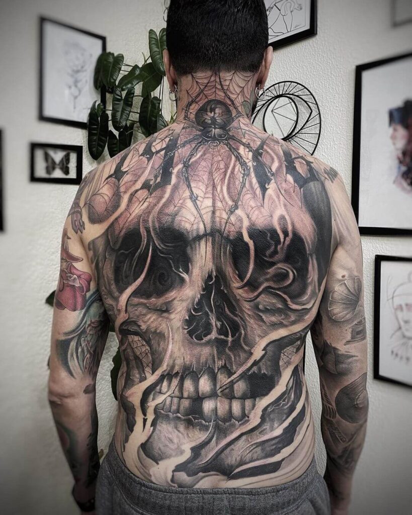 man with black and grey back piece, tattoo shows skull face and spider.