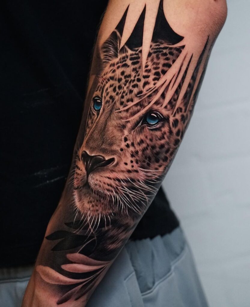 Forearm black and grey realism tattoo showing face of a leopard with blue eyes, hidden among leaves. 
