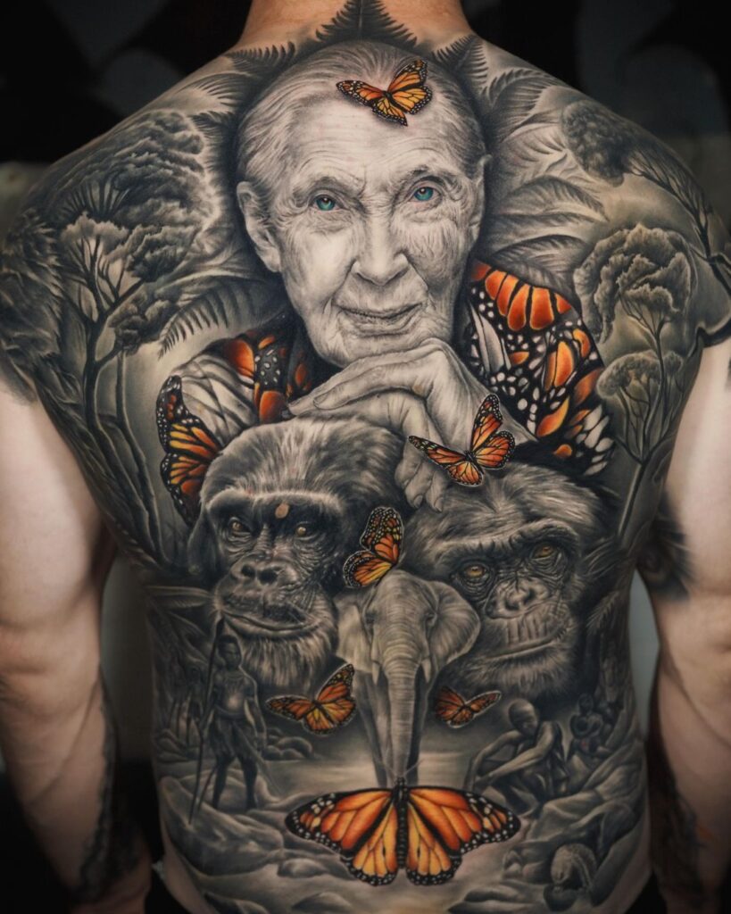 A black and grey realism backpiece showcasing a portrait of Dr Jane Goodall surrounded by chimps and trees and orange butterflies.