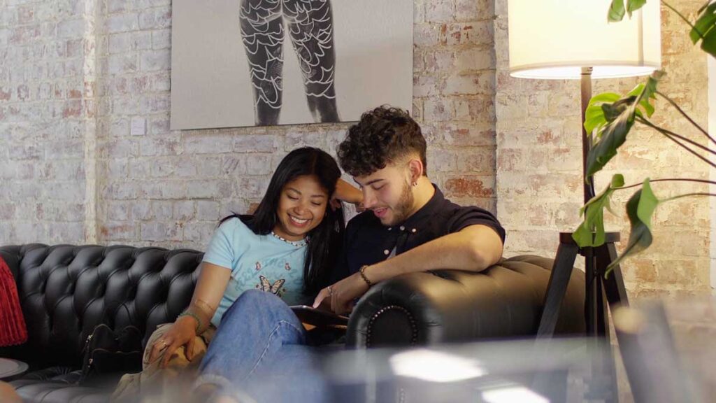 Image shows a smiling couple sitting on a sofa filling out a consultation form at No Regrets Bristol studio.