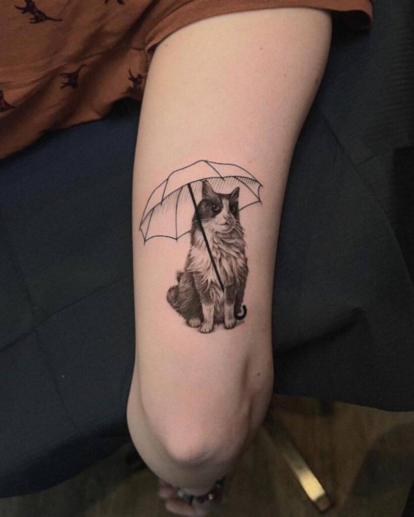 Micro -realistic black and grey pet portrait tattoo of a cat with an umbrella on its shoulder