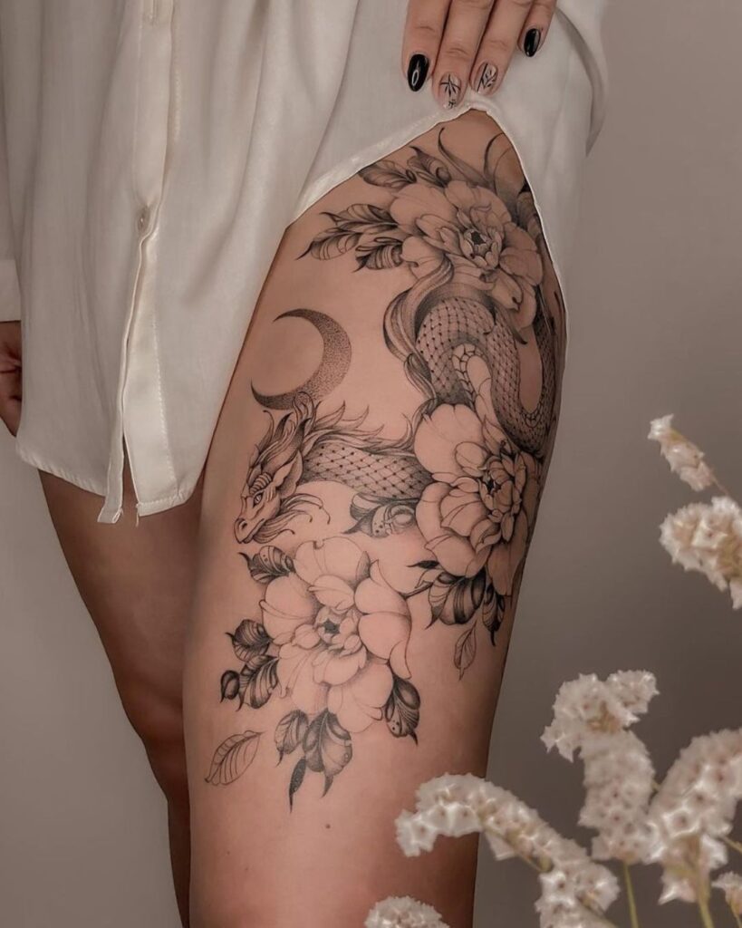 Thigh tattoo of a fine line, oriental dragon among peony flowers alongside a crescent moon