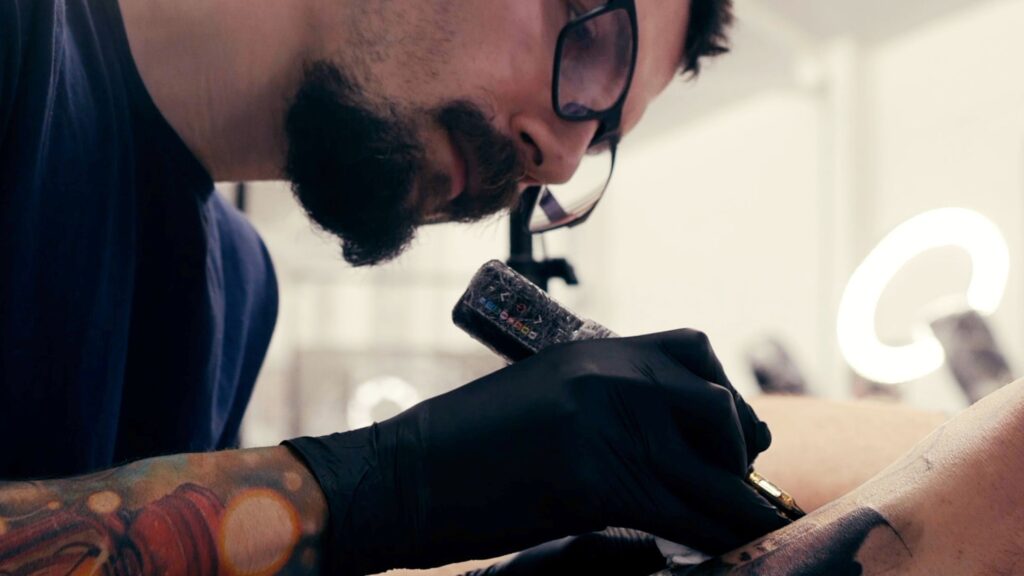 close up of man wearing glasses tattooing.