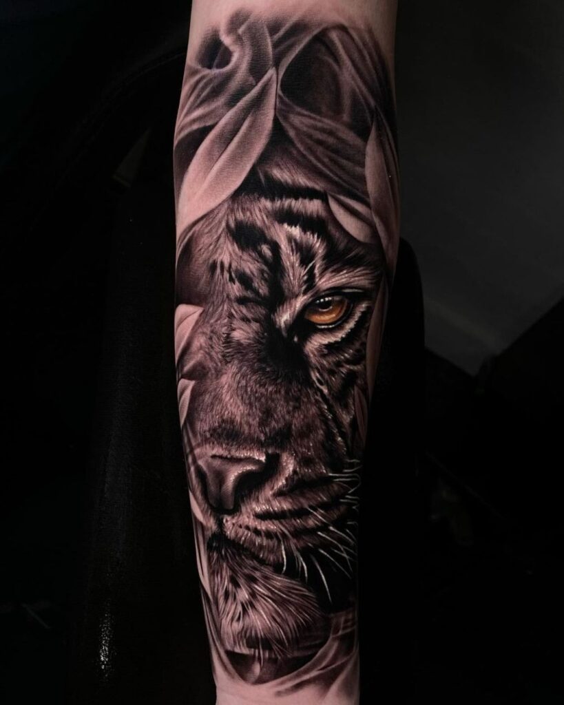 Forearm tattoo of realistic tiger face tattoo with amber eyes and leaves surrounding. Tattoo done by Andy Ramos, one of our resident artists at No Regrets Cardiff.